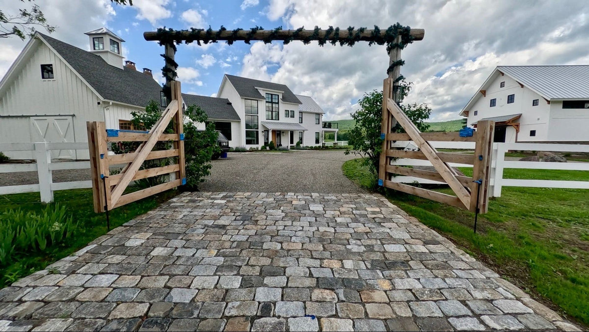 Reclaimed jumbo cobblestone driveway passing through a timber gate to white farm buildings at Bell Hill Farm