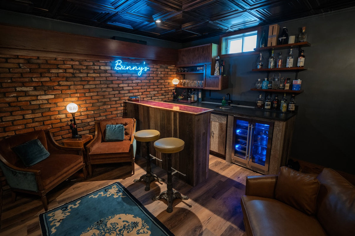 Home speakeasy bar with a reclaimed thin brick wall, neon sign and leather armchairs