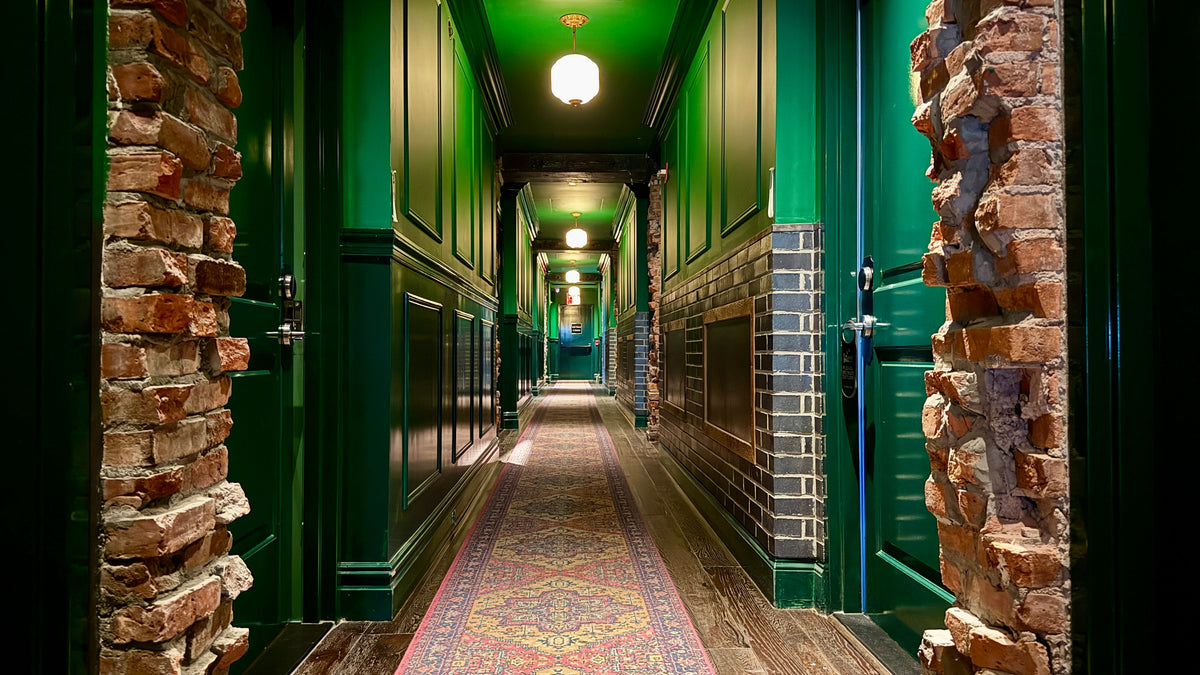 Sohotel hallway in Manhattan with green walls, a patterned runner and exposed reclaimed brick